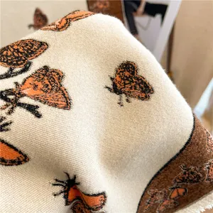 Detailed macro view of beige cashmere-feel shawl featuring orange butterfly and fringe