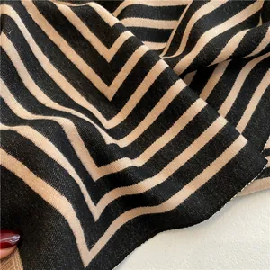 Gros plan sur la texture à chevrons géométriques de l'écharpe en noir et beige kaki
