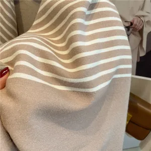 Close-up of the soft cashmere-like knit fabric with camel and white stripes and fringes