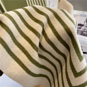 Gros plan détaillé sur la texture rayée vert et crème de l'écharpe en maille douce