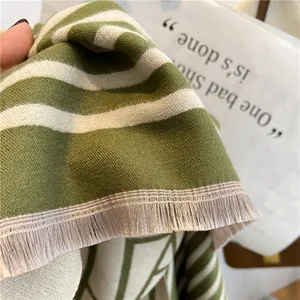Gros plan d'une écharpe rayée vert et beige en faux cachemire avec des franges fines