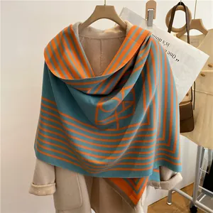 Détail de l'écharpe à rayures géométriques bleu et orange avec franges sur un manteau beige