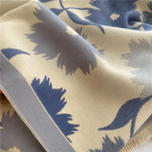Détail d'une écharpe épaisse beige avec motif de feuilles bleues et franges douces