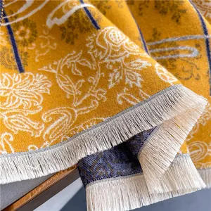 Macro detail of ginger yellow paisley scarf featuring fine woven texture and off-white tassels