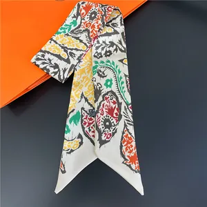 Detail of a paisley print skinny silk scarf displayed near a luxury orange gift box