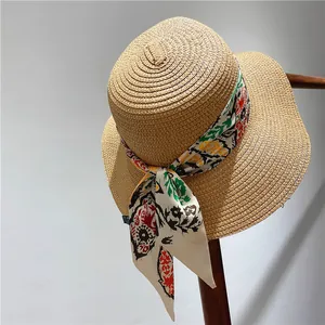Flat top straw hat in light khaki with floral scarf ribbon on a wooden stand