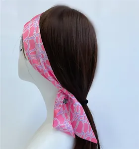 Detailed close-up of a pink floral silk scarf tied as a headband on a brunette model