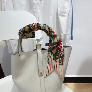 Detail of multi-color silk scarf wrapped around handle of cream leather bucket bag