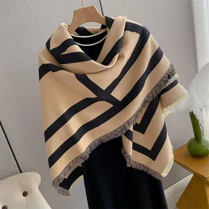 Detail of camel and black geometric stripe scarf with soft fringe on a wooden hanger