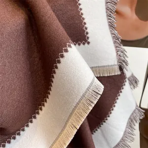 Détails du motif géométrique et des pompons sur un châle doux au toucher cachemire