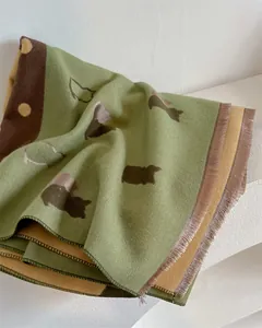 Detailed view of knitted scarf fringe and minimalist cat pattern in green and yellow