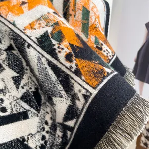 Close-up of geometric knit shawl showing orange and green jacquard weave with tassels