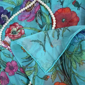 Détail d'un foulard carré en georgette turquoise avec imprimé floral et roulotté