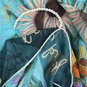 Artistic blue sunflower silk scarf with delicate pearl necklace decoration on a flat surface
