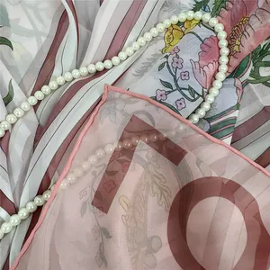 Dettaglio di sciarpa in seta floreale con bordi arrotolati e collana di perle
