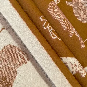 Detail van jacquard sjaal met eekhoornpatroon en zachte franjes in crème en okergeel