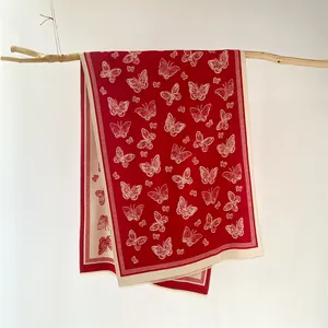 Detail view of red winter scarf with white butterfly prints hanging on a wooden branch