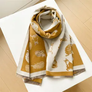 Detail van gebreide mosterdgele en crèmekleurige sjaal met kattenpatroon en franjes