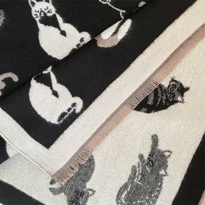 Detail van een gebreide sjaal met zwart-wit kattenjacquard patroon en fijne franjes