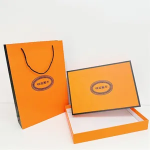 Vista detallada de la caja de regalo naranja gruesa y bolsa a juego con asas negras