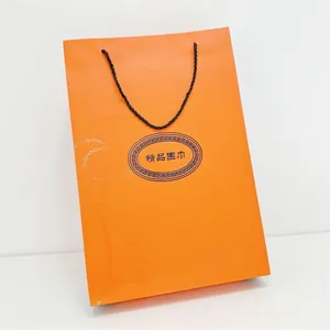 Detalle de una bolsa de regalo naranja con asas de cuerda negra y textura de cadena