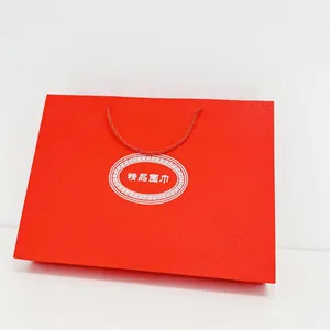 Detalle de la bolsa de regalo roja para bufanda con papel texturizado y asas trenzadas