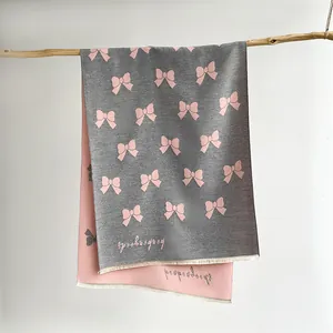 Close-up of double-sided knit scarf with pink and grey bow pattern and fringed edges