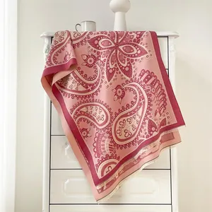 Châle pashmina à motif paisley rose et bordeaux drapé élégamment sur un meuble blanc