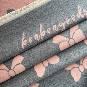 Close-up of gray scarf fabric with pink bow jacquard, script text and fringe detail