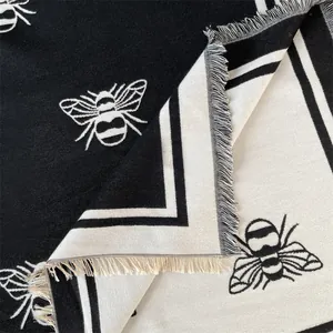 Macro detail of bee pattern scarf showing reversible black and white knit with fringe edge