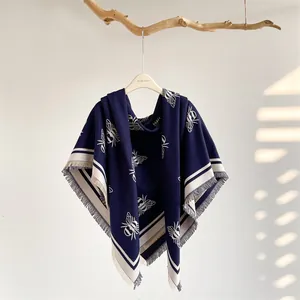 Close-up of navy blue pashmina with white bee patterns and tassels on a wooden hanger