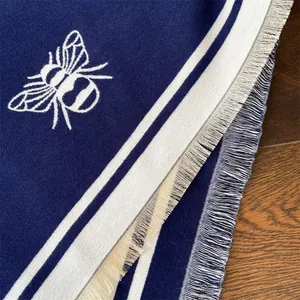 Close-up of navy blue winter shawl featuring white bee pattern and fringed edges