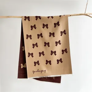 Close-up of beige bow-patterned scarf with white fringe tassels and soft cashmere texture
