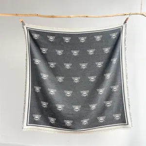 Detail of bee pattern square scarf with tassels hanging on a wooden branch