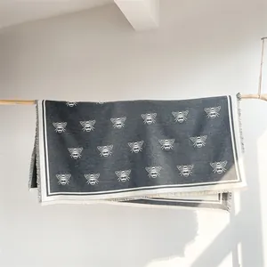 Detail of soft gray cashmere-style scarf with white bee patterns on a wooden rack