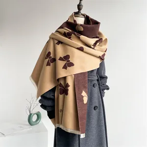 Detail of camel and brown shawl with bow patterns and fine fringe on grey coat
