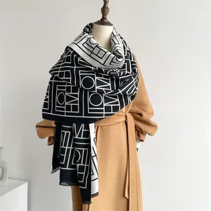 Détail d'une écharpe en maille géométrique noir et blanc drapée sur un manteau en laine camel