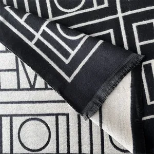 Gros plan du motif jacquard géométrique et des pompons sur l'écharpe en cachemire réversible