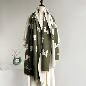 Detailed view of thick knit scarf with dark green bow jacquard pattern and fringe edge