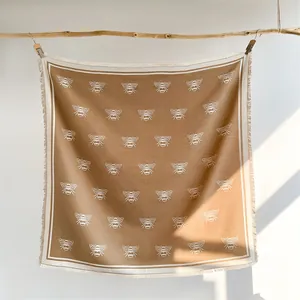 Detail of soft camel cashmere-like scarf with white bee patterns and fringe edges