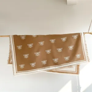 Detail of caramel brown cashmere scarf with white bee pattern and elegant fringe edges