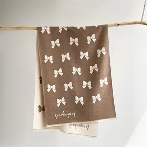 Brown and cream double-sided knitted scarf with white bow patterns and brand logo