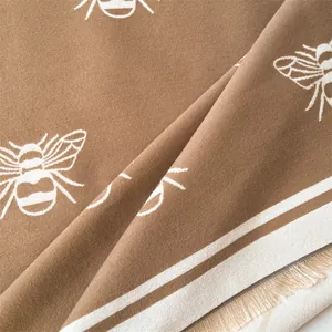 Detail view of brown cashmere shawl showing soft texture, bee patterns and fringe edges