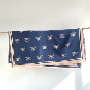Detailed view of navy cashmere-feel scarf featuring pink bee prints and fringe edges