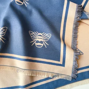 Close-up of cashmere-style shawl with bee patterns, navy and beige tones, and fringe details