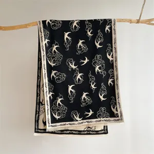 Detail of black and white cashmere-like scarf with swallow and cloud patterns on a branch