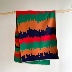 Close-up of thick knitted scarf with colorful wavy patterns hanging on a wooden branch