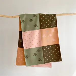 Detailed shot of cashmere-like scarf featuring bee prints, color blocks, and fringe edges