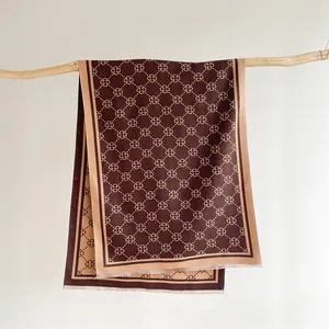 Close-up of brown clover monogram scarf hanging on a rustic wooden branch detail