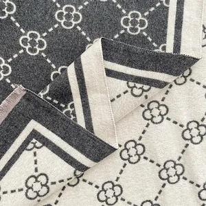 Detail of double-sided knit scarf with grey clover pattern and tassel trim texture